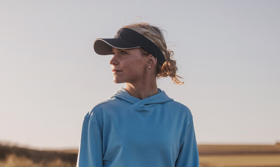 A woman in profile with blond hair. She has a navy golf shade and a light blue golf hoodie. 