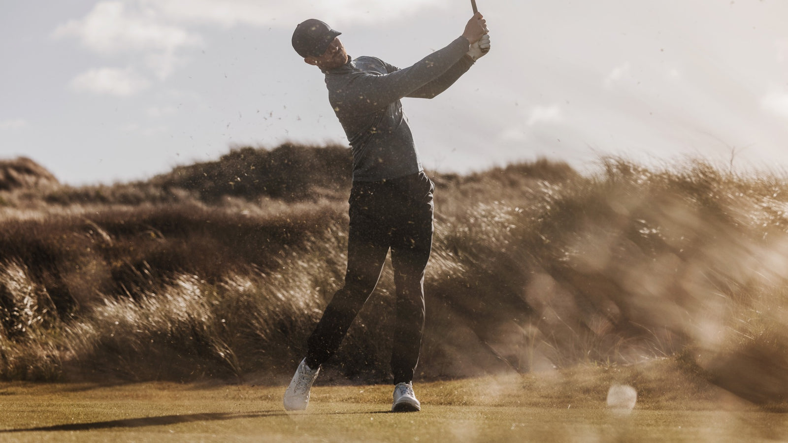 A golfer in performance golf clothes is hitting the ball so hard that the grass is flying around. 