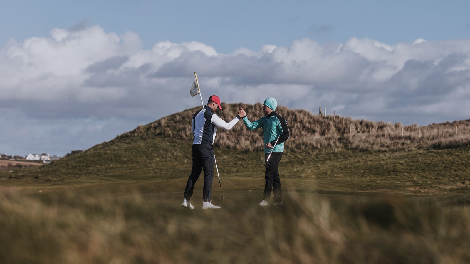 Two golfers are high-fiving on a golf course. They are wearing golf hats and golf caps in bright colors.