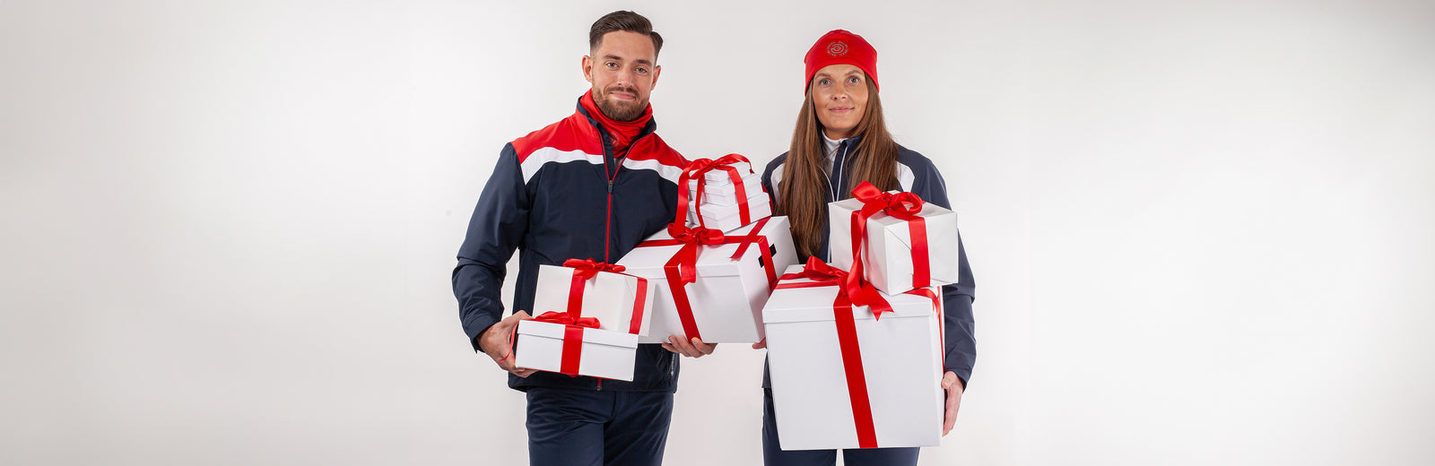 A happy man and women in matching golf clothing is holding 8 white boxes wrapped with shiny red ribbon. 